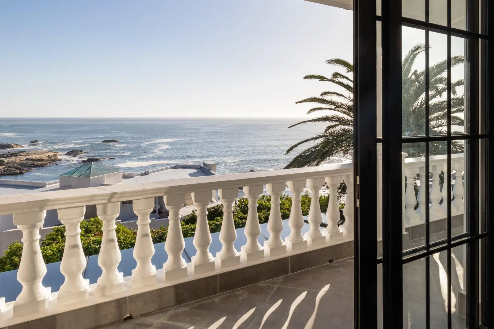 Balcony balustrade with the sea, rocks and rooftops beyond and a palm on the right