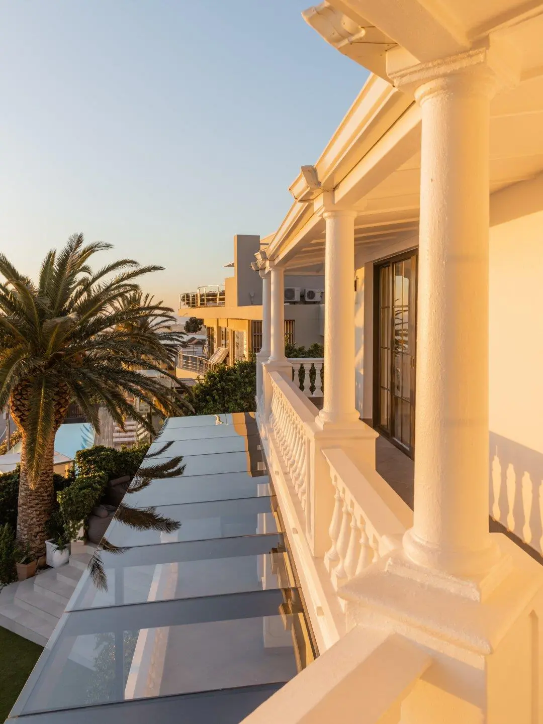 Balcony columns and balustrade in golden evening light, with a palm tree and a glass roof below