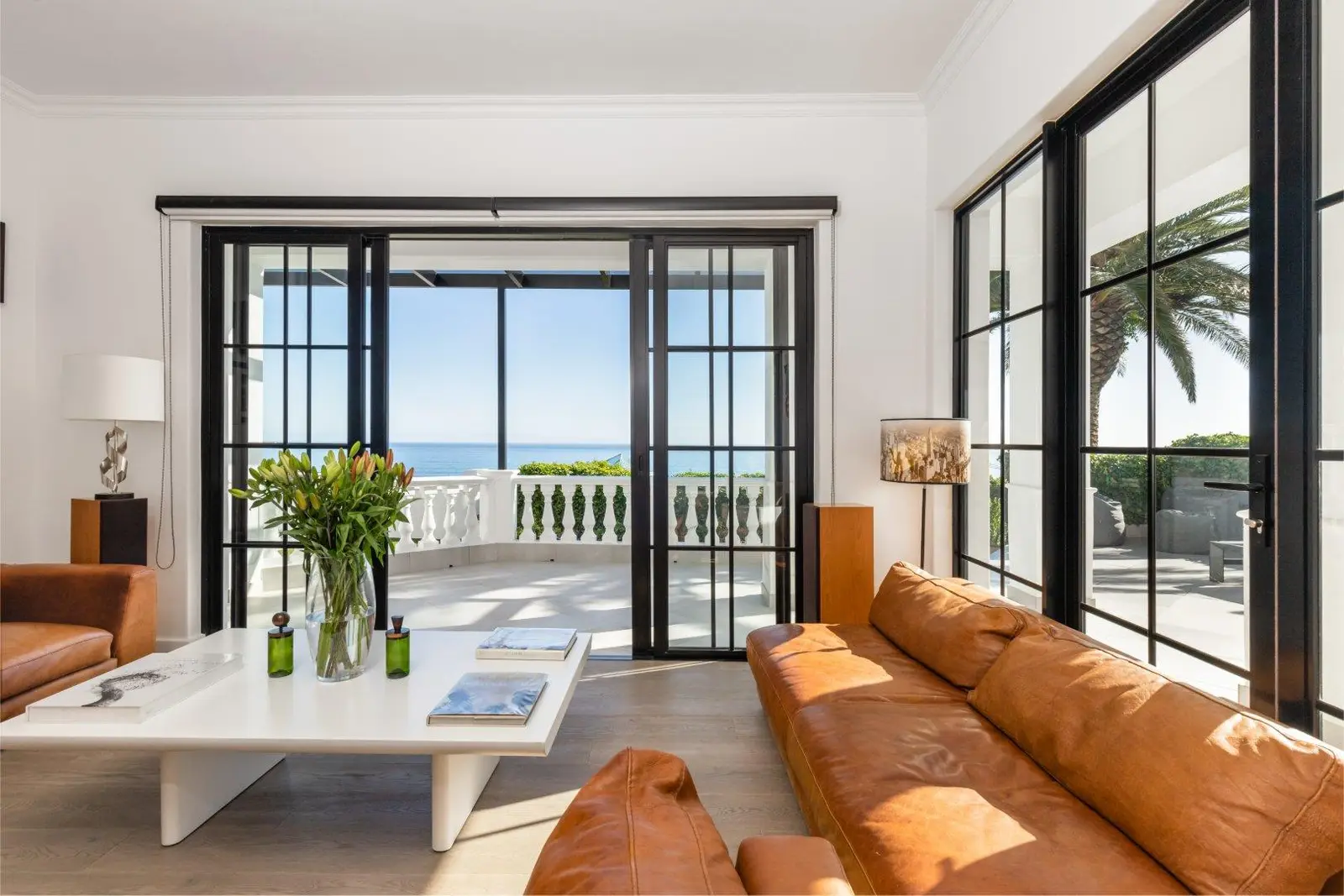 Living room with tan leather sofas and sliding glass doors opening to a balcony and the sea